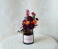 a wine bottle with flowers in it sitting on a white tablecloth covered round surface