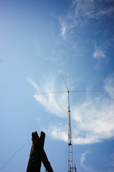 a very tall antenna on top of a wooden pole under a blue sky with wispy clouds