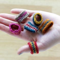 a person's hand holding five small crocheted rings in different colors and sizes