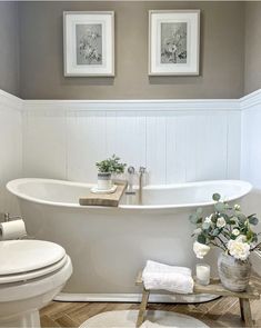 a white bath tub sitting next to a toilet under two framed pictures on the wall