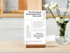 a vase filled with white flowers sitting on top of a wooden table next to a sign