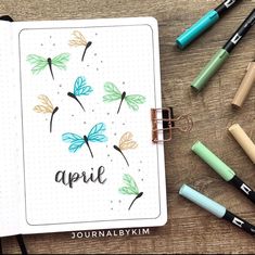 an open notebook with the word april written on it, surrounded by markers and pens