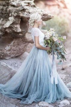 a woman in a blue dress is standing on some rocks and looking at the sky