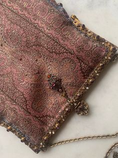 a pink and gold paisley design purse on a white surface with a chain attached to it