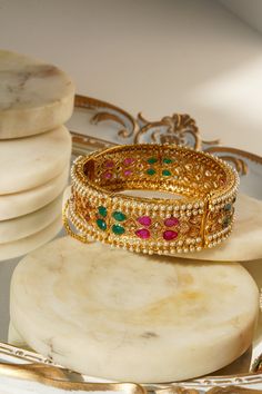 Introducing the Amika Bangle Set (Set of 2), a stunning addition to any jewelry collection. These gold-plated bangles feature intricate designs adorned with pearls and vibrant multicolor stones, including green and ruby accents. The detailed floral and petal patterns exude elegance and sophistication, making these bangles & bracelets set perfect for desi weddings and special occasions. The Amika Bangle Set showcases the timeless beauty of Navratan craftsmanship. The bangles are designed with an Festive Meenakari Round Bangle, Festive Gold Plated Meenakari Bangle, Festive Gold Meenakari Bangle, Elegant Multicolor Cutdana Bangle, Traditional Multicolor Cutdana Bangle, Gold Plated Bangles, Bangles Bracelets, Bangle Bracelet Set, Bracelets Set