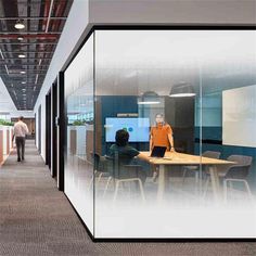 an office cubicle with glass walls and people walking around the room on either side