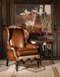 an old chair in front of a cow painting and table with vases on it