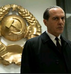 a man in a suit and tie standing next to two gold emblems