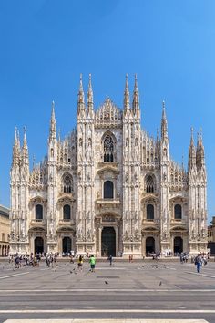 many people are walking around in front of a large building with tall spires and towers