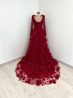 a red wedding dress with long sleeves and flowers on the skirt is displayed in front of a white wall