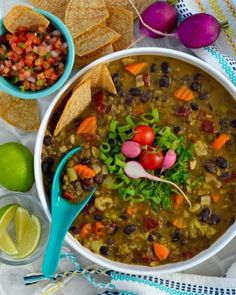 a bowl of soup with tortilla chips on the side and limes next to it