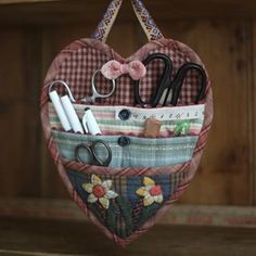 a heart shaped purse with scissors and other items in it hanging from a hook on a wooden shelf