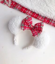 a white poodle wearing a red plaid bow on it's head next to a blanket