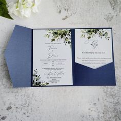 the wedding stationery is set on top of a blue envelope with white flowers and greenery