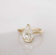 a yellow gold ring with a pear shaped diamond in the center, on a white surface