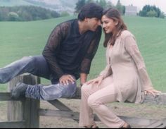 a man and woman sitting on top of a wooden fence in front of a field