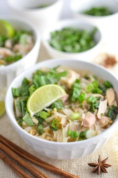 two bowls filled with noodle soup and garnished with green onions, carrots, and lime