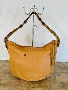 RARE UNIQUE LIMITED EDITION  Vtg Rare Coach Ergo stud rivet camel Shoulder bag  PREOWNED, still IN GOOD CONDITION camel color Thick premium pebble leather Ziptop closure  Solid brass and silver hardware/ tassel  Purple sateen Lining  a zip pocket with Coach Creed Tag  Approx. Measurements:  12-17" L x 11" H x 5.25" plus D strap drop 8.5" Clean interior  ALL ITEMS ARE 100% AUTHENTIC GUARANTEE few blemishes shown in pictures  PLEASE ASK QUESTIONS BEFORE CHECKOUT  SORRY NO CANCELLATIONS/NO RETURNS Leather Satchel Shoulder Bag With Rivets, Brown Leather Bags With Rivets, Yellow Leather Bags With Metal Hardware, Leather Shoulder Bag With Rivets For Daily Use, Daily Use Leather Shoulder Bag With Rivets, Brown Leather Hobo Bag With Metal Hardware, Leather Shoulder Bag With Rivets, Everyday Leather Shoulder Bag With Rivets, Coach Ergo