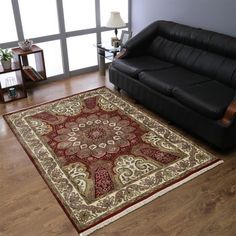 a living room with a black leather couch and red rug on the wooden flooring