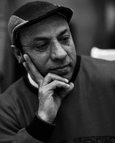 a black and white photo of a man with his hand on his chin looking at the camera