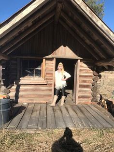 a woman standing in the doorway of a small log cabin with her dog sitting on the porch