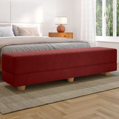 a bed sitting on top of a wooden floor next to a red footstool