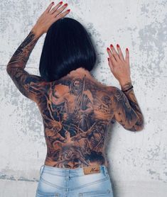 a woman with tattoos on her back and hands behind her head, leaning against a wall