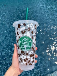 a hand holding up a starbucks cup in front of the blue water with leopard print on it