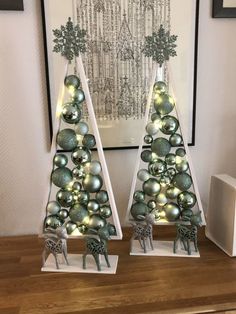 two christmas trees with ornaments on them sitting next to each other in front of a painting