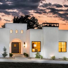 a white house is lit up at night with the sun setting in the sky behind it