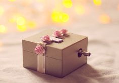 a small box with flowers on it sitting on top of a bed next to some lights