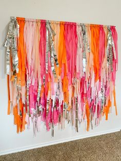 there are many ribbons hanging on the wall with clothes pins attached to it and one is pink, orange, and silver