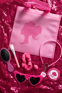 a pink bag, sunglasses, hair brush and other items are laying on a sequined surface