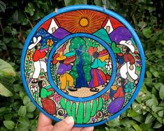 a hand holding up a colorful plate in front of some plants and bushes with an image of people on it