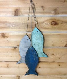 two wooden fish hanging from strings on a wood paneled wall, one blue and the other green