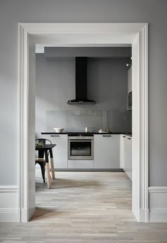 a kitchen with white walls and wood flooring next to an open doorway leading into the dining room