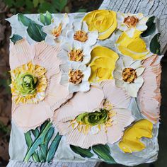 an art piece with flowers painted on it sitting on top of a wooden table next to leaves