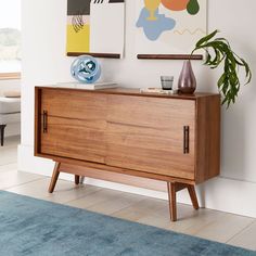 a wooden cabinet with two paintings on the wall and a potted plant in front of it