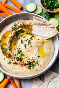 hummus in a bowl with pita chips and cucumbers on the side