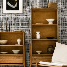 two wooden shelves with dishes and bowls on them in front of a wallpapered wall