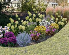 the garden is full of colorful flowers and plants in front of a large house with trees