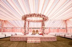 an outdoor wedding setup with pink and white drapes on the ceiling, decorated with flowers