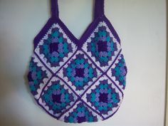 a crocheted bag hanging on the wall in front of a white door with purple handles