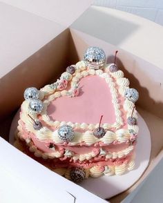 a heart shaped cake in a box with decorations on it's edges and pink frosting