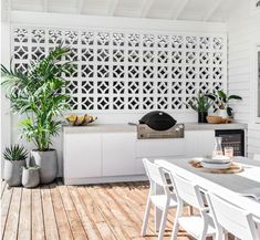 an outdoor kitchen with white furniture and potted plants on the counter top, next to a grill