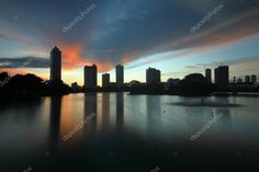 the sun is setting behind some buildings on the water and clouds are reflected in the water