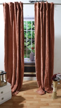 an open window with curtains in front of it and a vase on the floor next to it