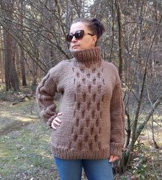 a woman standing in front of some trees wearing a sweater and jeans with her hands on her hips