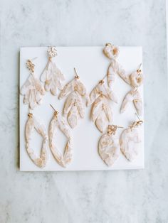 six pairs of leaf shaped earrings on a white marble slab with gold earwires