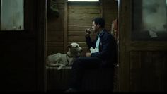 a man sitting on a bench next to a dog in a room with wood paneling